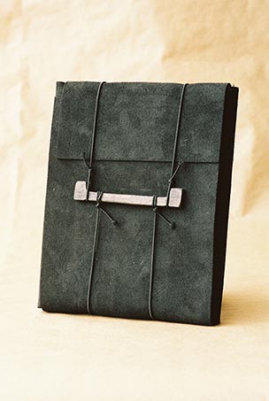 Couverture du livre. Cuir noir entourer de ficelles retenues par un morceau de bois.
