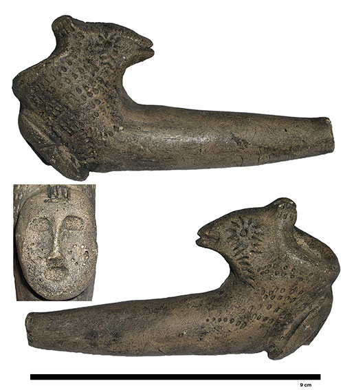 Bowl and shank of a double-headed pipe, with a human head and a bird head. The bird head faces the smoker. The pipe is shown sideways to clearly depict the bird-head form. The human head is shown head-on. The bowl is studded with small decorative marks. 