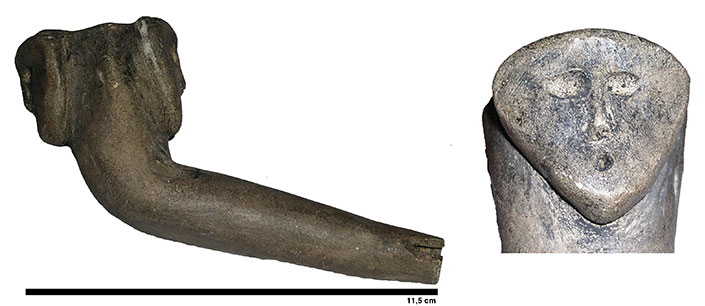 Bowl and shank of a pipe with double triangular human faces, viewed in profile. One of the heads faces the smoker. The other head, with a strong gaze, is depicted head-on.